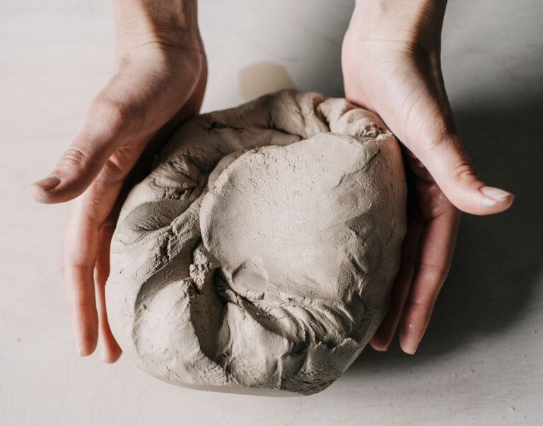 Female potter hands working with clay in workshop. White desk on background